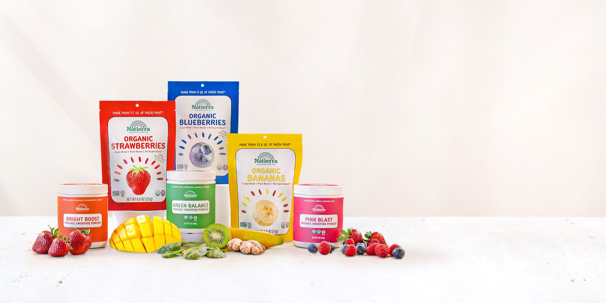 Large Photo of several packs of organic freeze-dried snacks and jars of organic smoothies  displayed on a white marble countertop with various fruits around