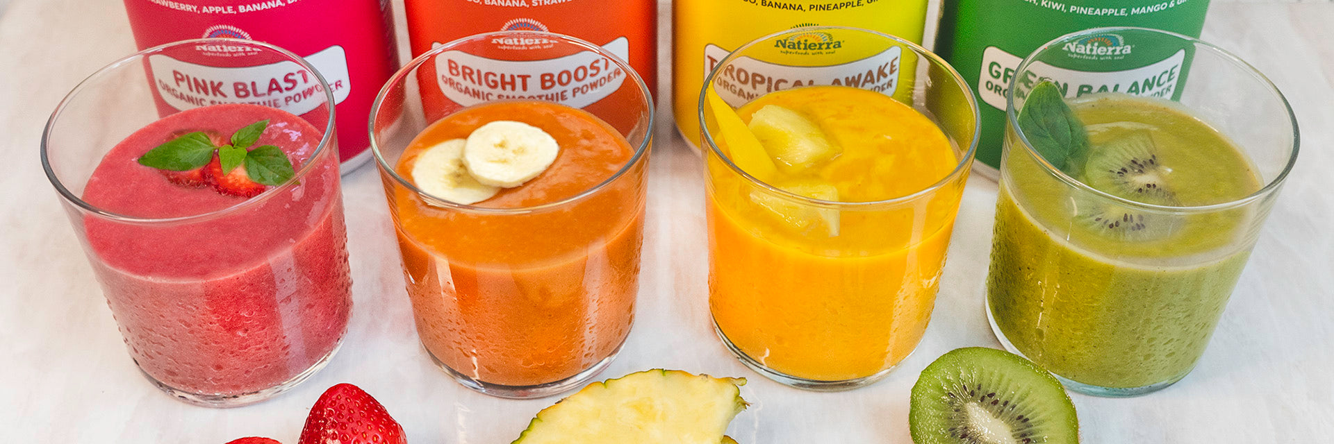 Four colorful smoothie drinks and Pink Blast, Bright Boost, Tropical Awake and Green Balance smoothie jar in background.