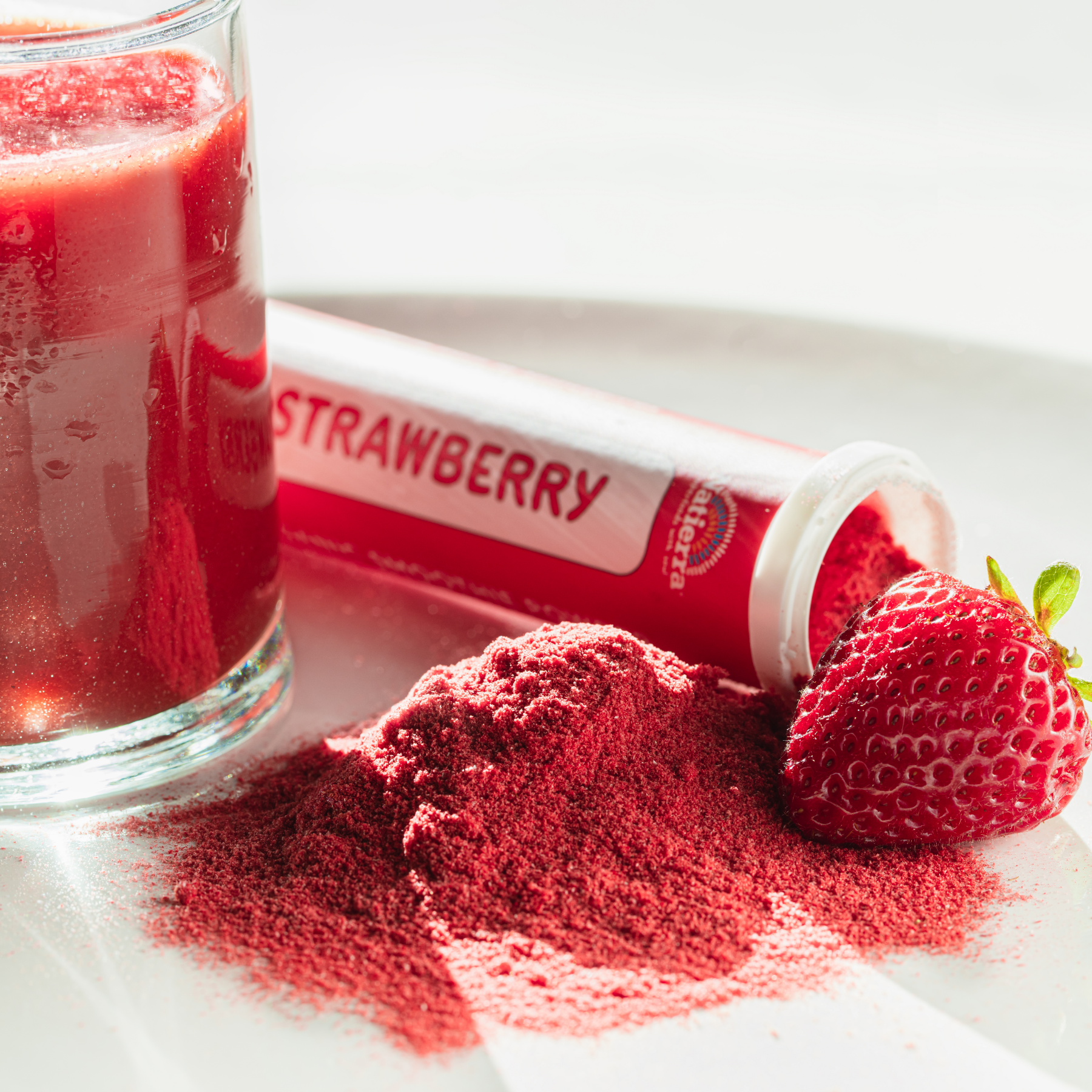 Open Natierra Strawberry Smoothie tube next to spilled powder, strawberry and smoothie in glass