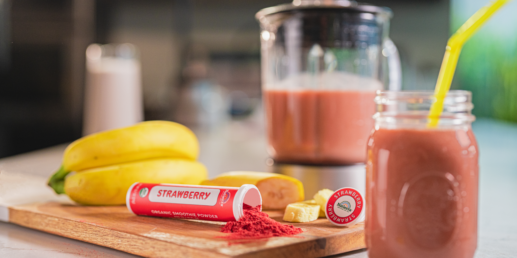Natierra Organic Strawberry smoothie tube spilled in a wood cutting board, with smoothie in mason jar and Bananas in the background
