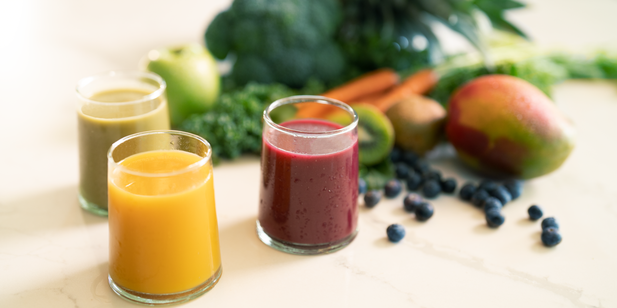 three glasses with variety of smoothie flavors and vegetables and fruits on the background