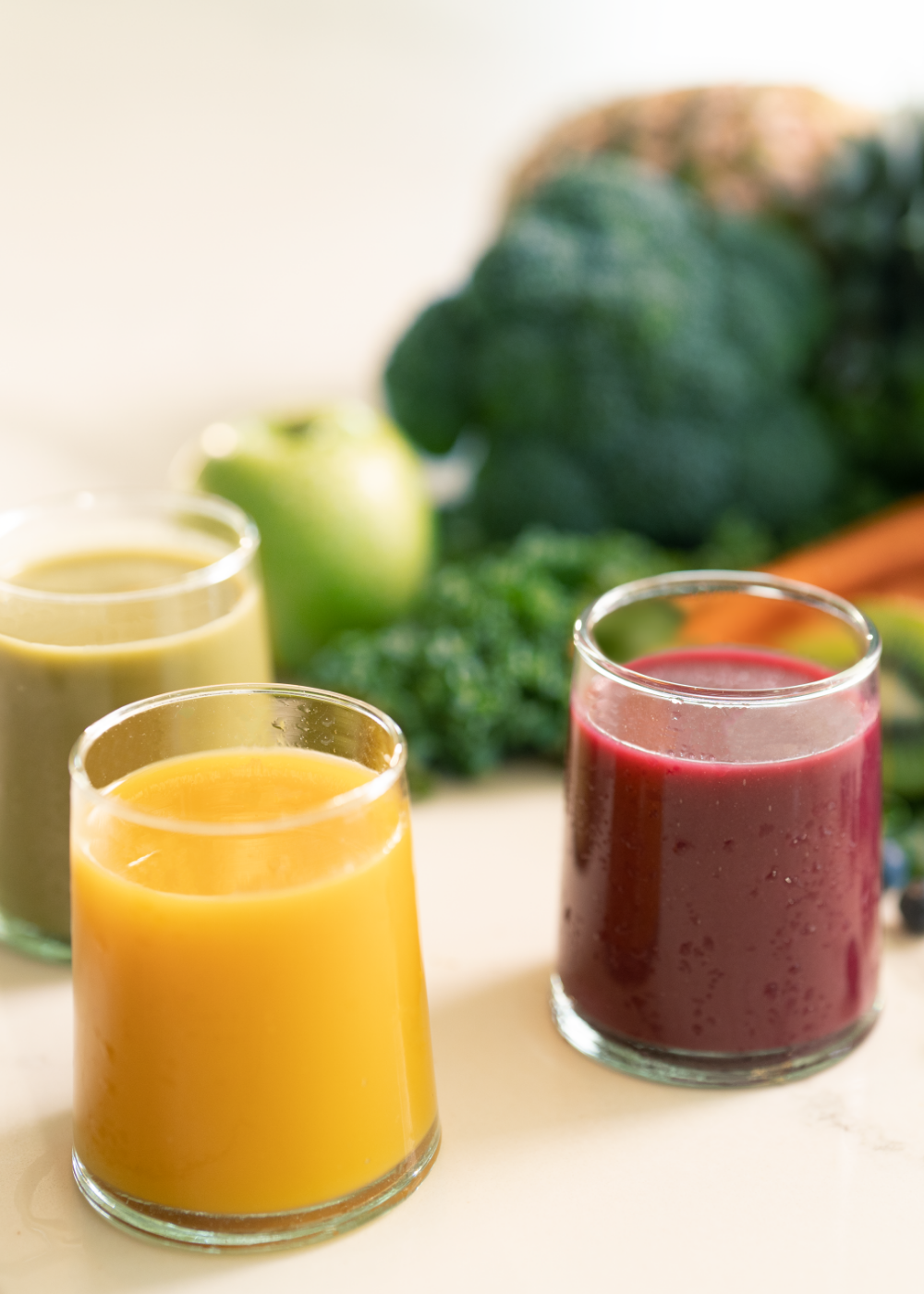 three glasses with variety of smoothie flavors and vegetables and fruits on the background