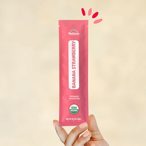 Individual stick pack of Natierra's Banana Strawberry Organic Smoothie held by a hand in front of a creme background