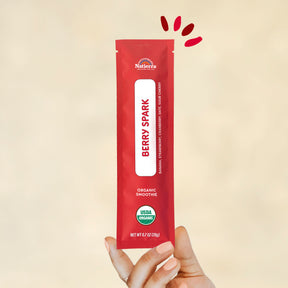 Individual stick pack of Natierra's Berry Spark Organic Smoothie held by a hand in front of a creme background
