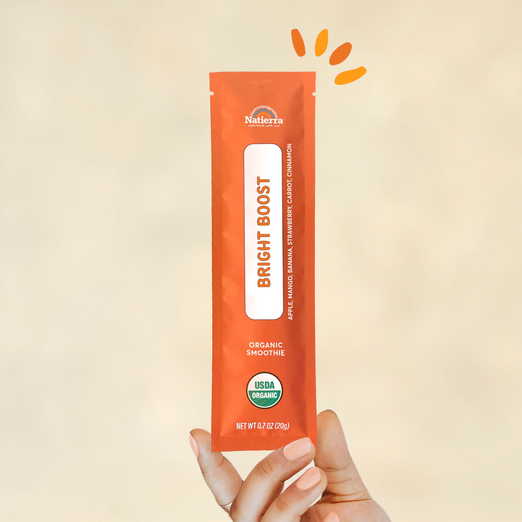 Individual stick pack of Natierra's Bright Boost Organic Smoothie held by a hand in front of a creme background