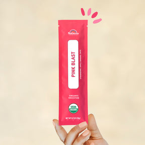Individual stick pack of Natierra's Pink Blast Organic Smoothie held by a hand in front of a creme background