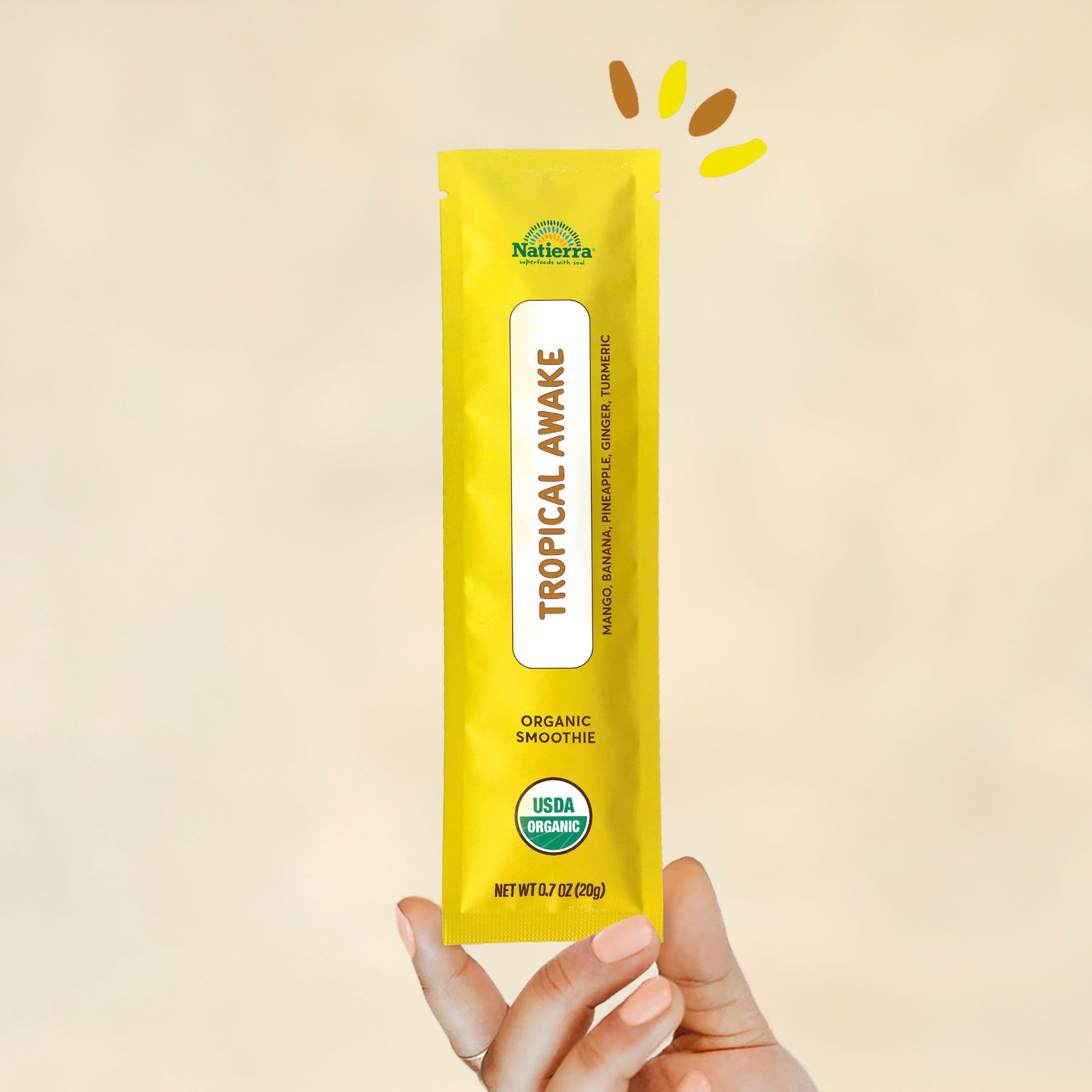 Individual stick pack of Natierra's Tropical Awake Organic Smoothie held by a hand in front of a creme background