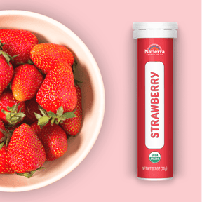 Natierra Organic Strawberry Smoothie Powder tube next to bowl of strawberries